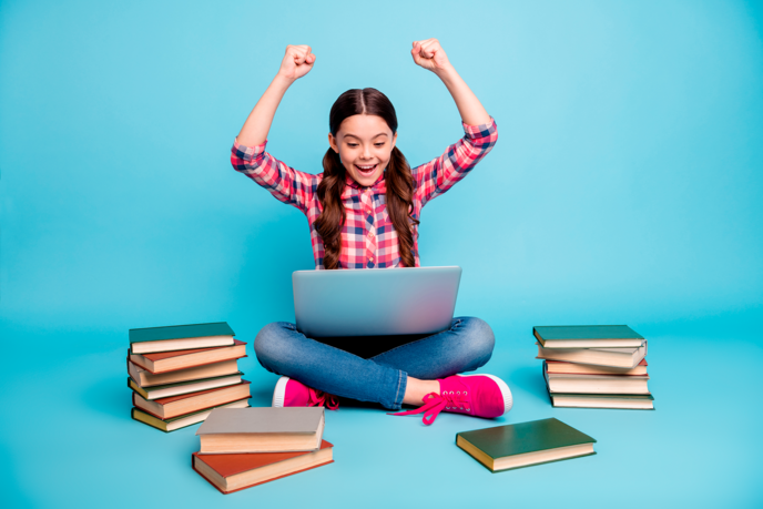En meget glad pige sidder og kigger på sit digitale skolebibliotek på en bærbar mens hun er omgivet af skolebøger.